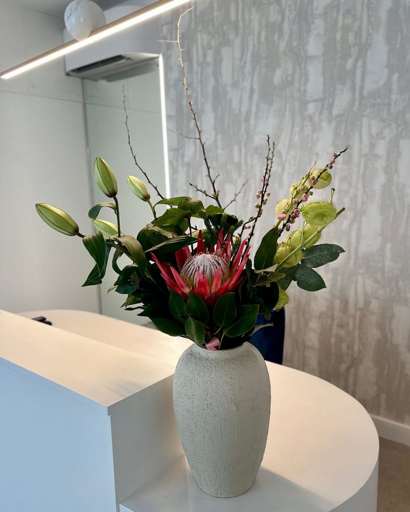 Protea and other flowers in a textured white vase on the curved white reception desk.